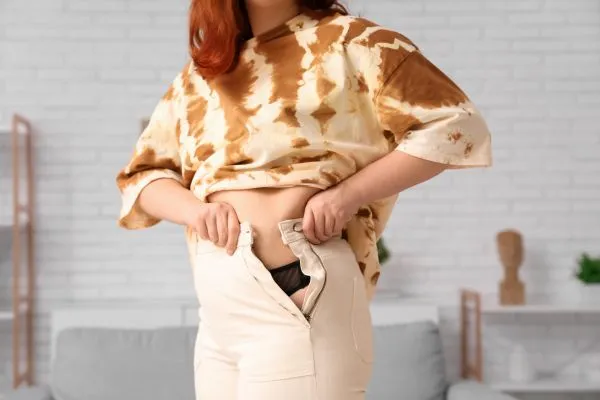 Image of woman trying to do her trousers up after pregnancy weight gain Tong