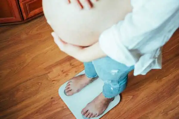 Image of woman weighing herself and experiencing weight gain through pregnancy Tong